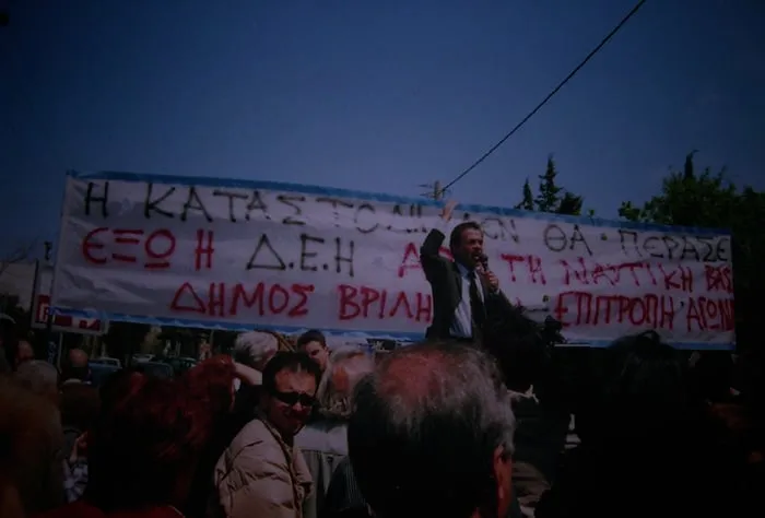 Άνδρας μιλά σε τηλεβόα σε διαμαρτυρία μπροστά σε πανό.