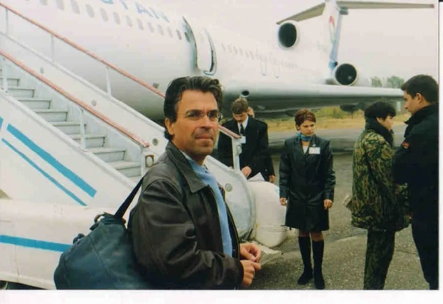 Ο Αργύρης Ντινόπουλος με σάκο στον ώμο στη σκάλα επιβίβασης αεροσκάφους, με πλήρωμα και επιβάτες γύρω του.