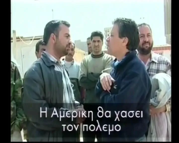 Ο Αργύρης Ντινόπουλος συζητά με ομάδα ανδρών σε δρόμο της Βαγδάτης, 2003. Υπότιτλος στο καρέ: «Η Αμερική θα χάσει τον πόλεμο».