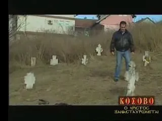 Ο Αργύρης Ντινόπουλος περπατά ανάμεσα σε λευκούς σταυρούς σε χορταριασμένο νεκροταφείο, αρκετοί γερμένοι ή σπασμένοι, με ξερά καλάμια, ένα κτίριο και σπίτια με κεραμοσκεπές στο βάθος. Κάτω δεξιά, ο ένθετος τίτλος της εκπομπής του «ΚΟΣΟΒΟ / Ο ΧΡΙΣΤΟΣ ΞΑΝΑΣΤΑΥΡΩΝΕΤΑΙ».