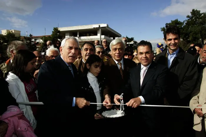 Κοπή κορδέλας με αρκετούς επισήμους και ένα κορίτσι μπροστά από σύγχρονο κτίριο, σε επίσημη ημερήσια τελετή.